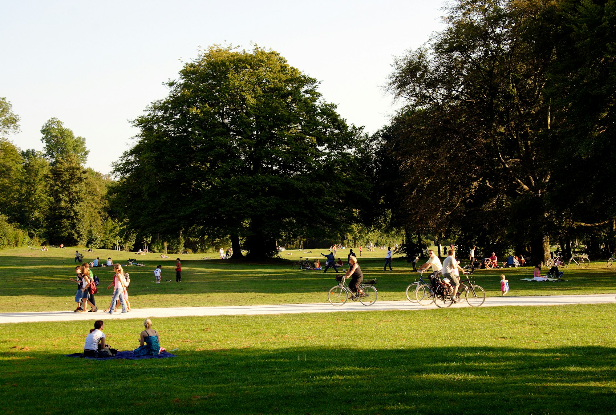 Many people enjoy the afternoon sun on the meadows of the English Garden, sitting and lying; others walk or ride a bicycle.