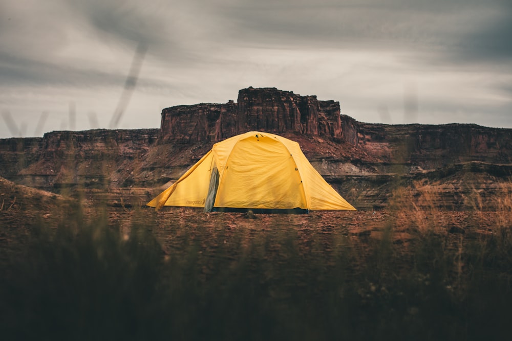 yellow dome tent on brown rock formation near body of water during daytime