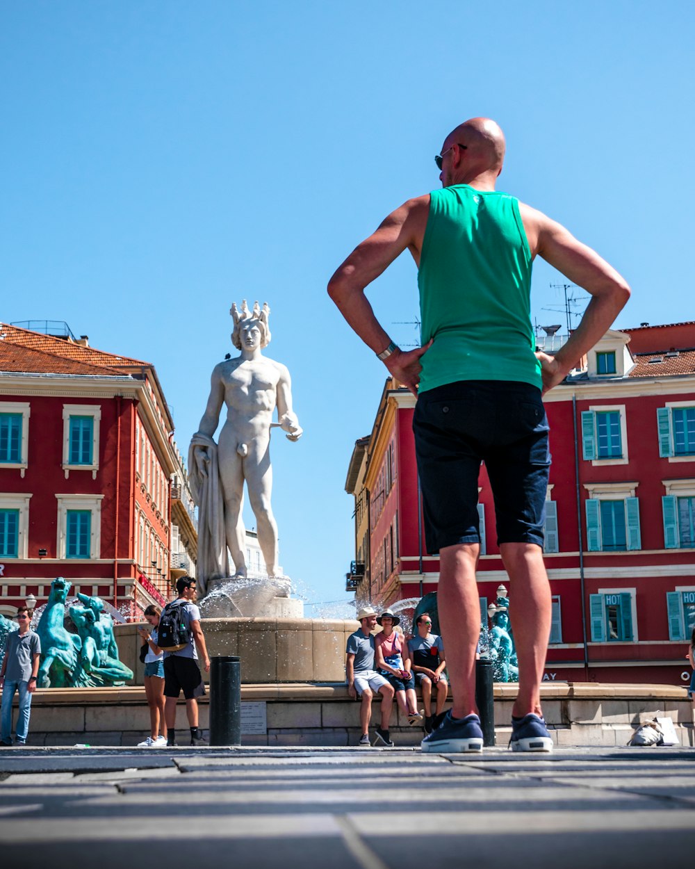 man in teal tank top and black shorts standing in front of statue