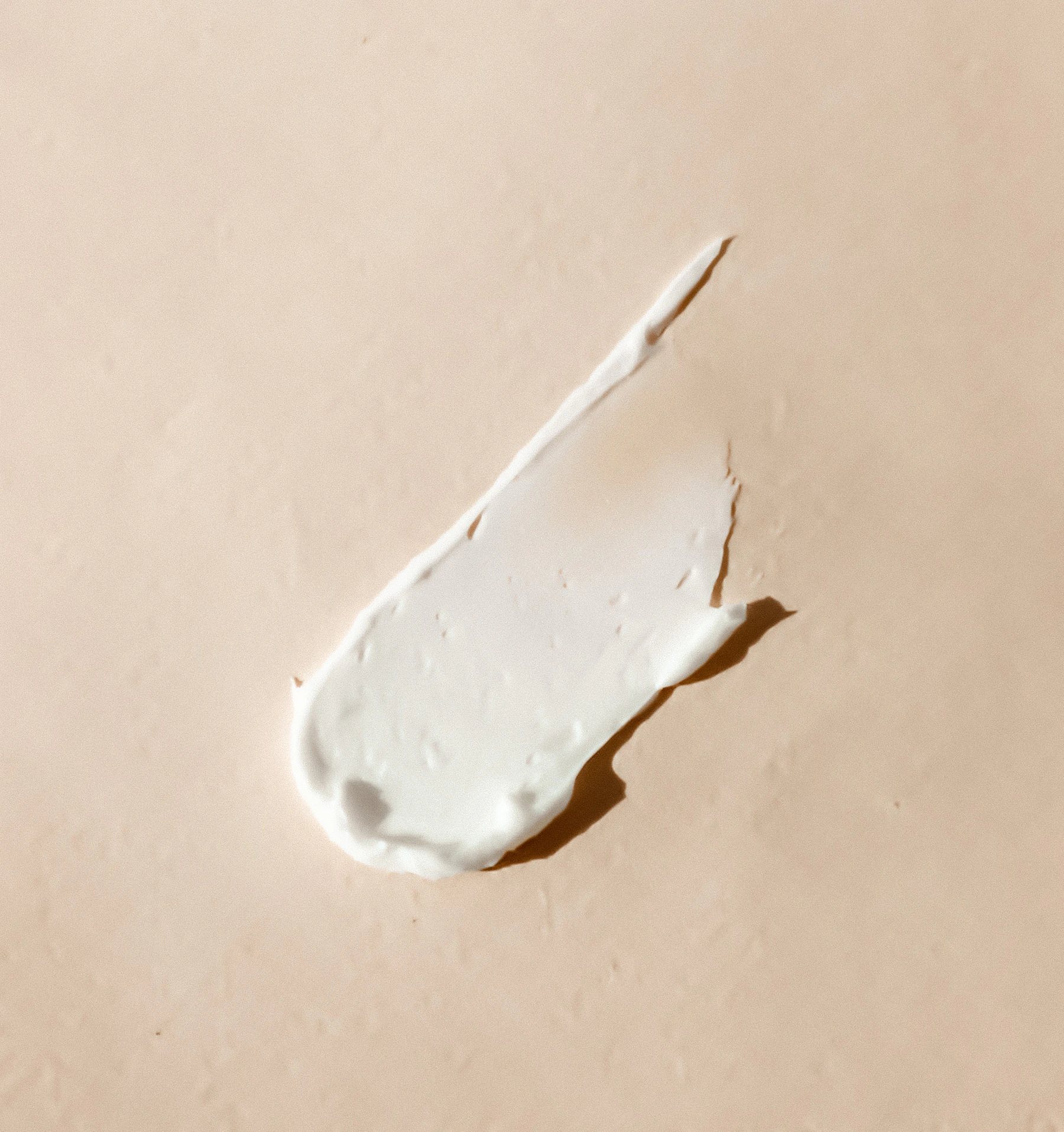 Smear of white moisturizing cream on a beige surface