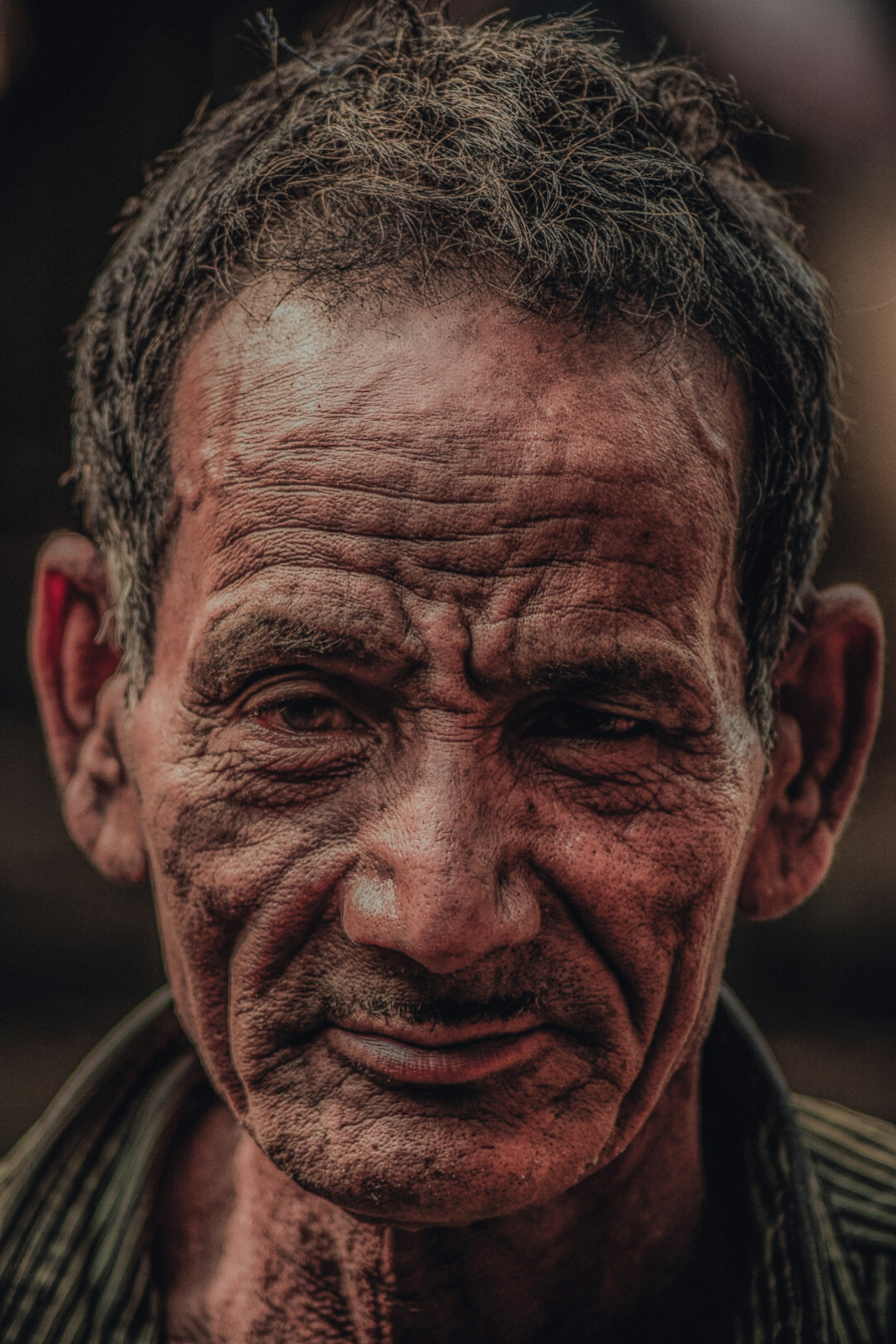 A candid street portrait of an elderly man with deep wrinkles and a gentle smile, bathed in warm afternoon light.