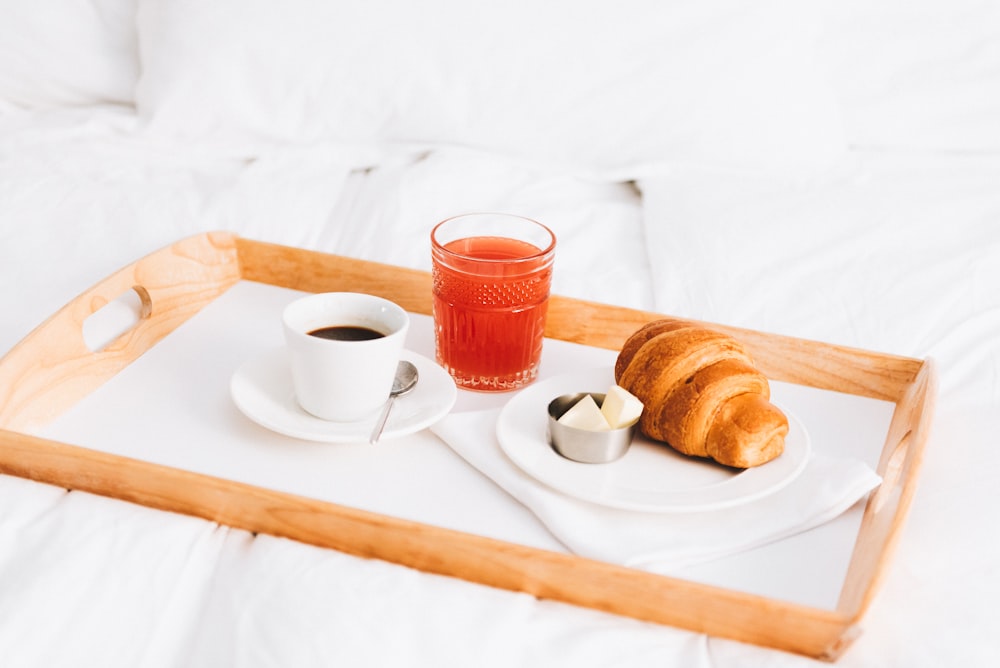 dos panes marrones en un plato de cerámica blanca junto a una taza de té de cerámica blanca sobre un mantel blanco