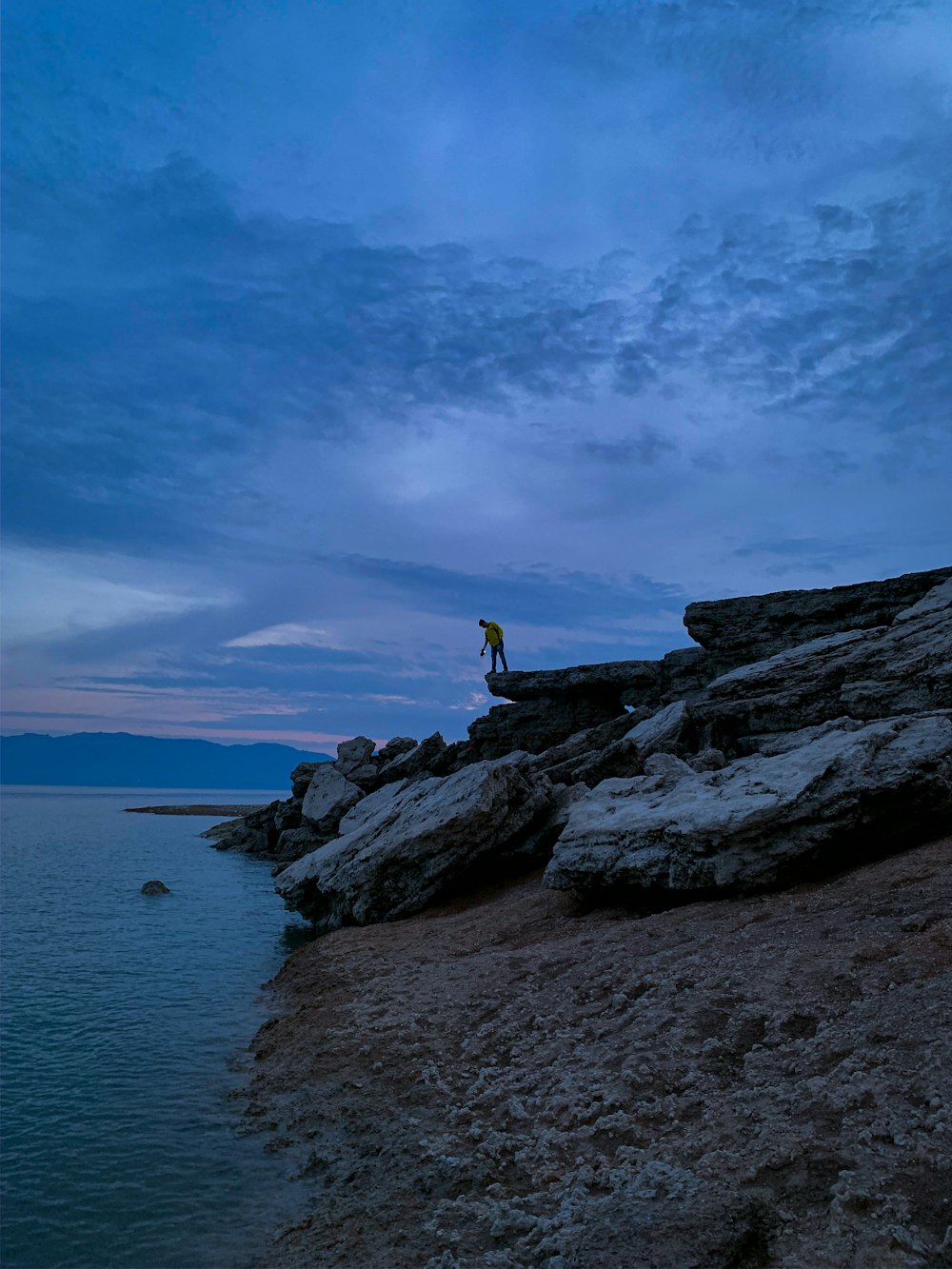 a man standing on top of a rocky cliff next to the ocean