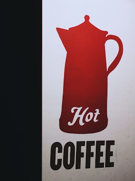 A graphic design featuring a red silhouette of a coffee pot with the word 'Hot' written in cursive script. Beneath the pot, the word 'COFFEE' is presented in bold, black uppercase letters on a light background. The design is simple and eye-catching with a strong contrast between the colors.