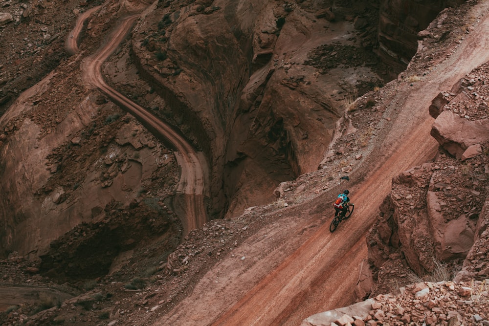 man in black jacket and blue denim jeans climbing brown rocky mountain during daytime