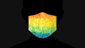 A silhouette of a person wearing a mask featuring a vibrant tie-dye pattern that includes shades of orange, yellow, green, and blue.