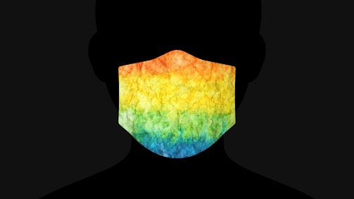 A silhouette of a person wearing a mask featuring a vibrant tie-dye pattern that includes shades of orange, yellow, green, and blue.