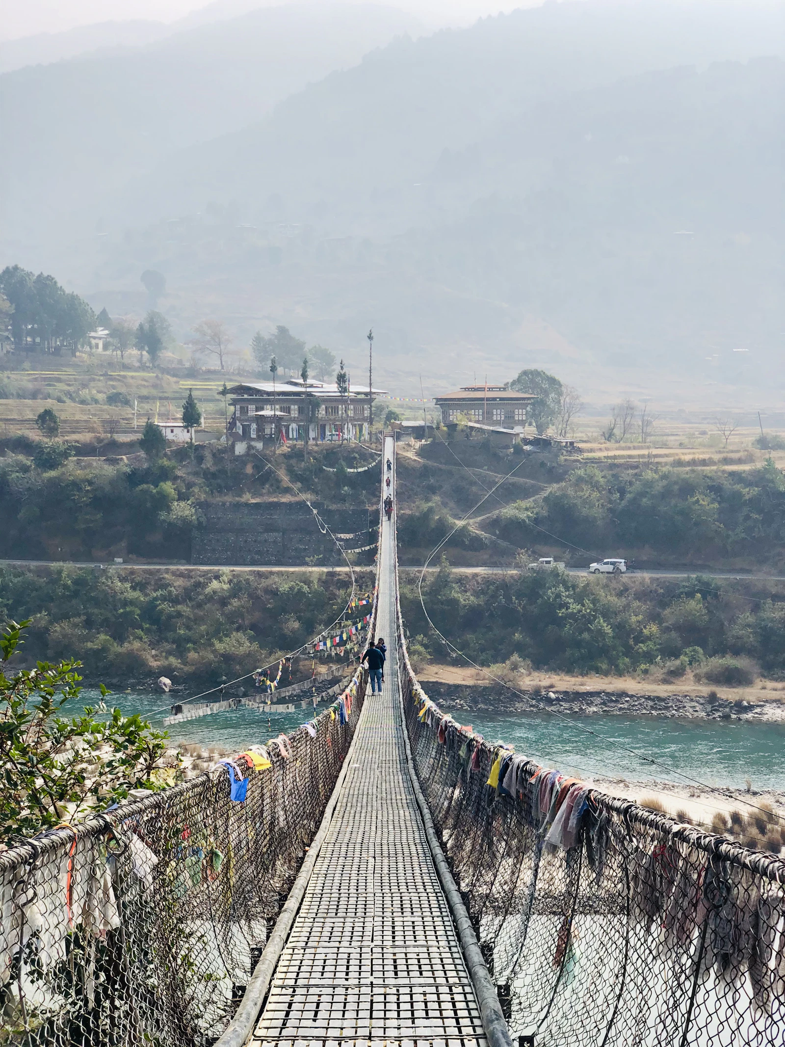 The long Punakha suspension bridge hung with prayer flags, running over the blue green river toward farmhouses