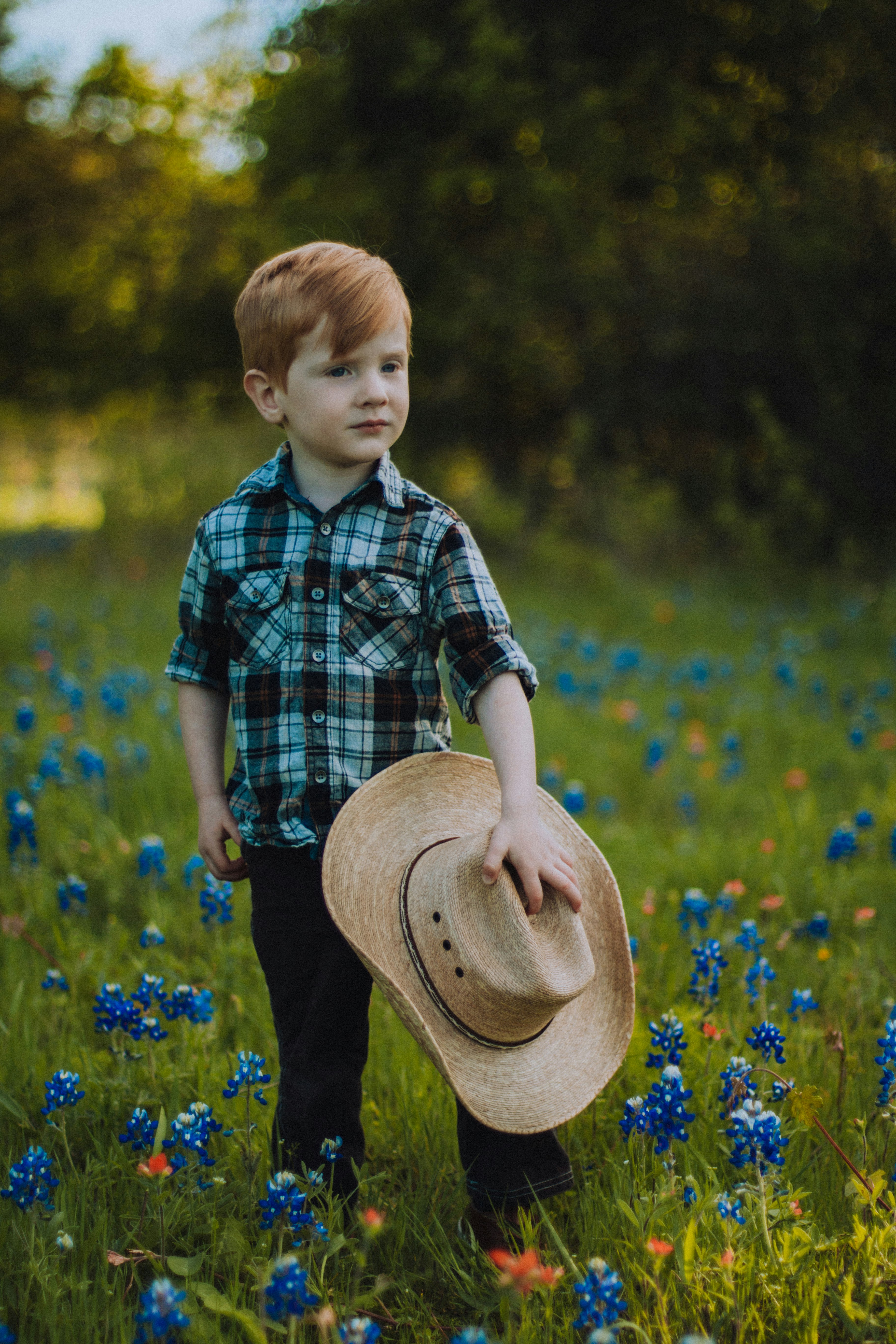 boy in blue and white plaid button up shirt wearing brown hat standing on yellow flower