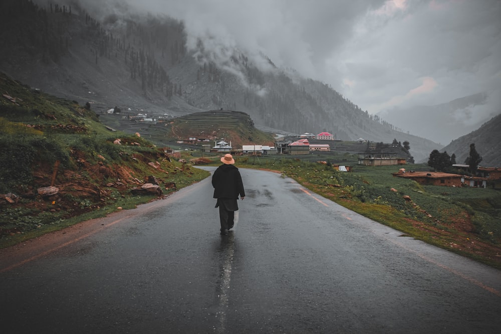 man in black jacket walking on gray asphalt road during daytime