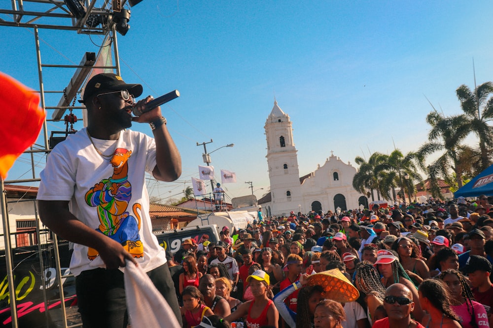 man in white t-shirt singing on stage during daytime