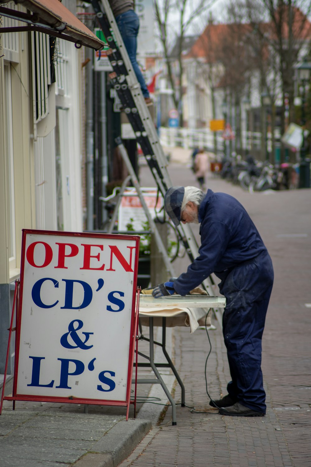 man in blue jacket and blue denim jeans standing beside white and red coca cola signage