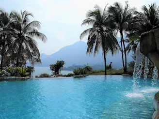 A serene Hawaiian poolside scene with crystal-clear water reflecting the sky, framed by tropical foliage.