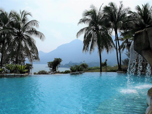 A serene Hawaiian poolside scene with crystal-clear water reflecting the sky, framed by tropical foliage.