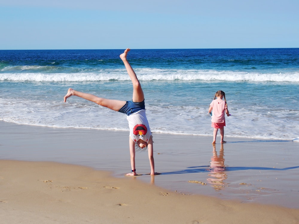 2 women in blue and black bikini jumping on beach during daytime