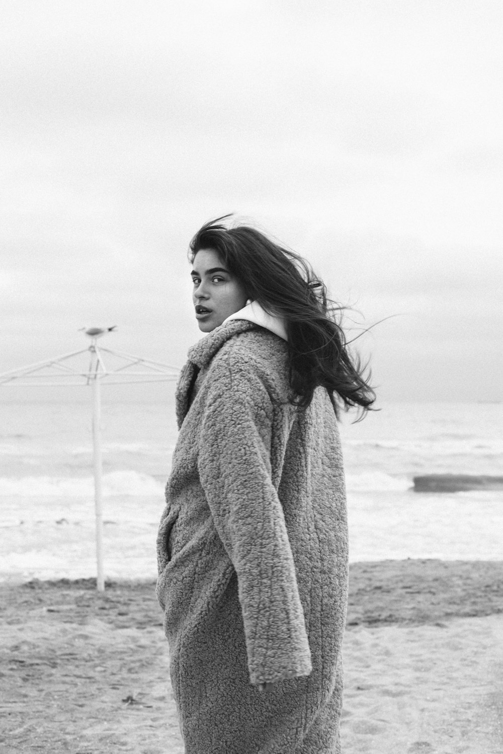 해변에 서 있는 스웨터를 입은 여자의 회색조 사진