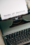 A vintage typewriter with black keys and white letters, with a sheet of paper inserted. The paper reads 'Terms of Service' in typewriter font.