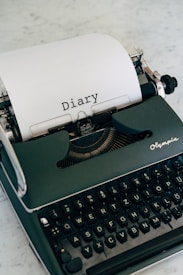 A vintage typewriter with a sheet of paper inserted, displaying the word 'Diary' typed in a classic font. The typewriter is placed on a marble surface and exudes a sense of nostalgia.