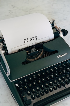 A vintage typewriter with a sheet of paper inserted, displaying the word 'Diary' typed in a classic font. The typewriter is placed on a marble surface and exudes a sense of nostalgia.