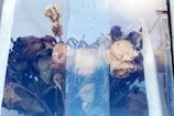 A collection of wilted and dried flowers placed behind a pane of glass. The flowers are predominantly brown and faded, likely indicating age or exposure to the elements. The glass has a slightly cloudy texture, adding to the overall mood of decay and nostalgia.