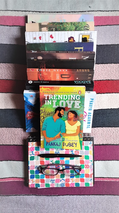 A vibrant flat lay of colorful ebooks stacked neatly with a pair of glasses and a notebook on a wooden table.