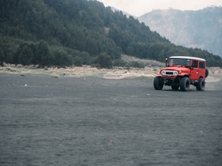 A 4WD jeep driving along volcanic terrain with Mount Batur glowing in early morning light.