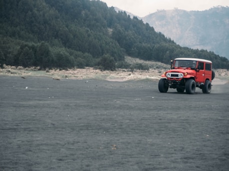 A 4WD jeep driving along volcanic terrain with Mount Batur glowing in early morning light.