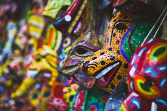A collection of vibrant, intricately painted animal masks displayed closely together. These masks feature vivid colors and patterns, including spots and stripes, reminiscent of wild animals like leopards and other creatures. The craftsmanship highlights detailed features like eyes, mouths, and ears, contributing to their artistic appeal.