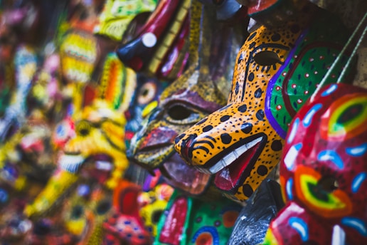 A collection of vibrant, intricately painted animal masks displayed closely together. These masks feature vivid colors and patterns, including spots and stripes, reminiscent of wild animals like leopards and other creatures. The craftsmanship highlights detailed features like eyes, mouths, and ears, contributing to their artistic appeal.