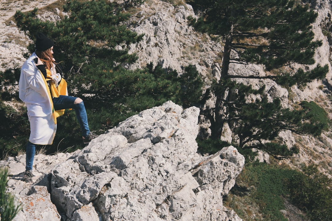 man in yellow shirt and blue denim jeans standing on rocky hill during daytime