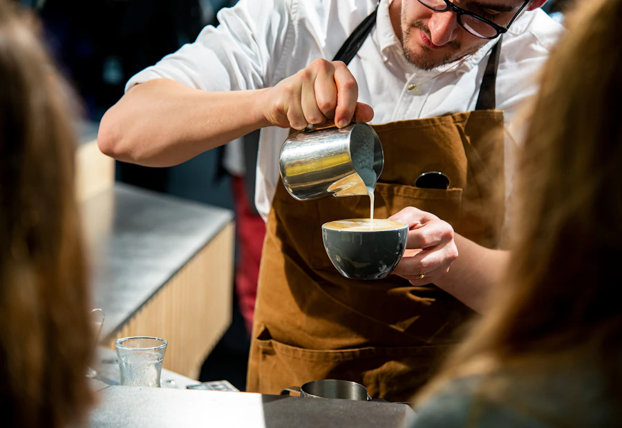 Barista mengenakan celemek kanvas AFUN berwarna cokelat tanah sambil menuang latte art