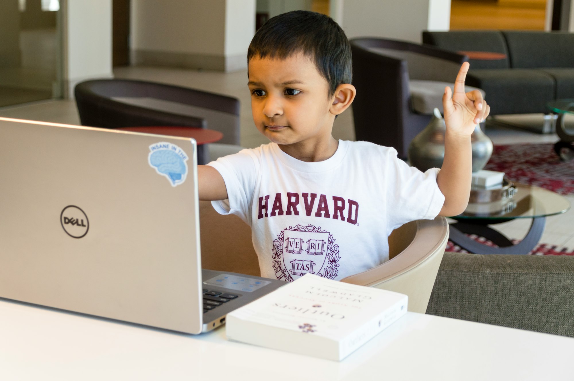 Young boy in front of laptop raising his hand.