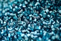A close-up view of shiny, cylindrical, metallic-looking beads or pellets. They have a reflective surface and are arranged in a dense, overlapping pattern, creating a visually textured and intricate composition.