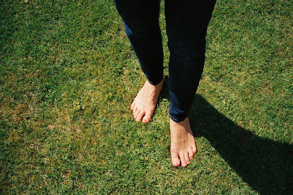 pessoa em jeans azuis em pé no campo verde da grama