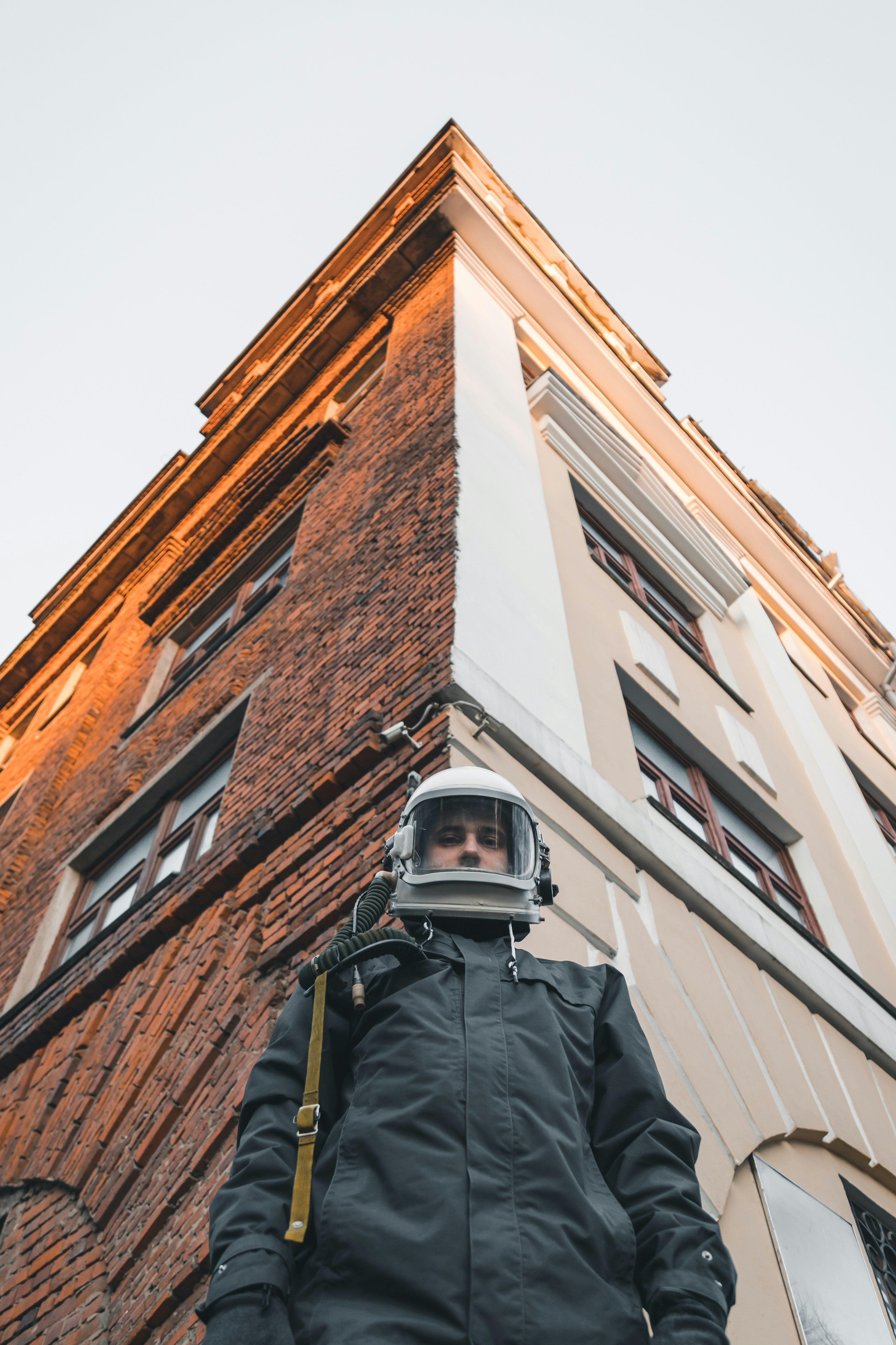 man in black jacket wearing white helmet standing in front of brown concrete building during daytime