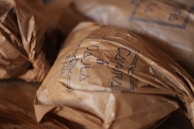 Crinkled brown paper packages are neatly arranged on a wooden surface. The packages have handwritten text on them, possibly denoting a brand, with a clear, simple stamp-like design.