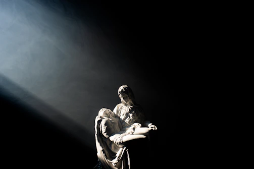 A white marble sculpture of a woman holding a man in a dark room