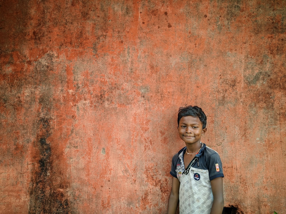 boy in white and black polo shirt standing beside red wall