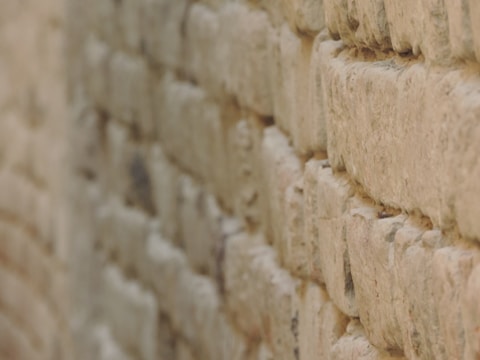 A close-up view of a textured stone wall, showcasing the rough and uneven surfaces of the stones. The image captures the intricate details of the masonry work, with stones stacked in a staggered pattern to form a sturdy structure.