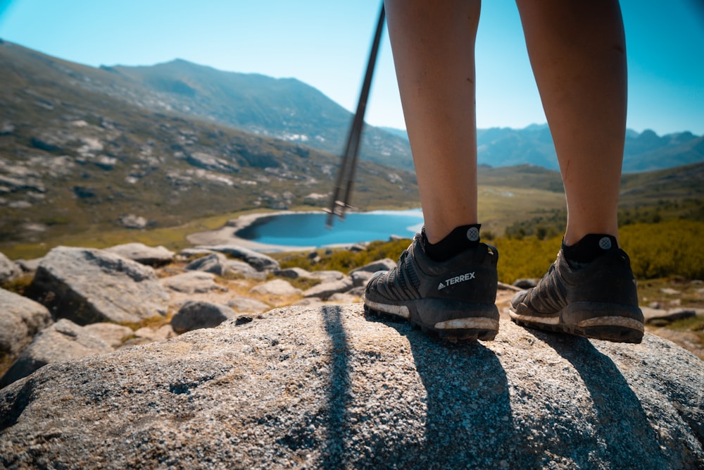 person wearing black hiking shoes standing on rocky ground during daytime