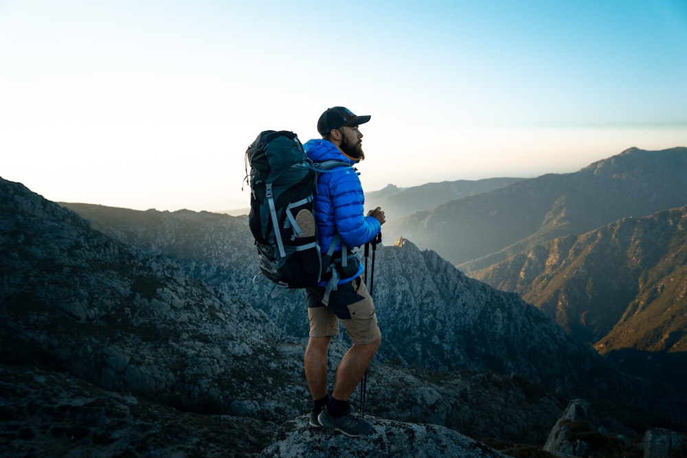 Hombre en mochila azul y negra de pie en la formación rocosa durante el día