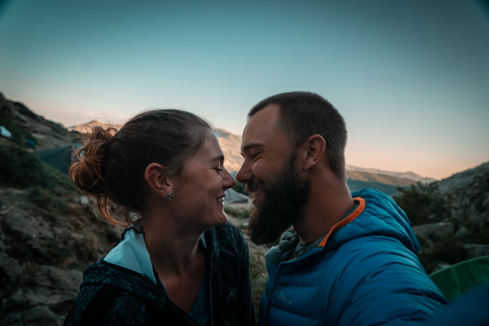 man in blue hoodie kissing woman in black and gray shirt during daytime