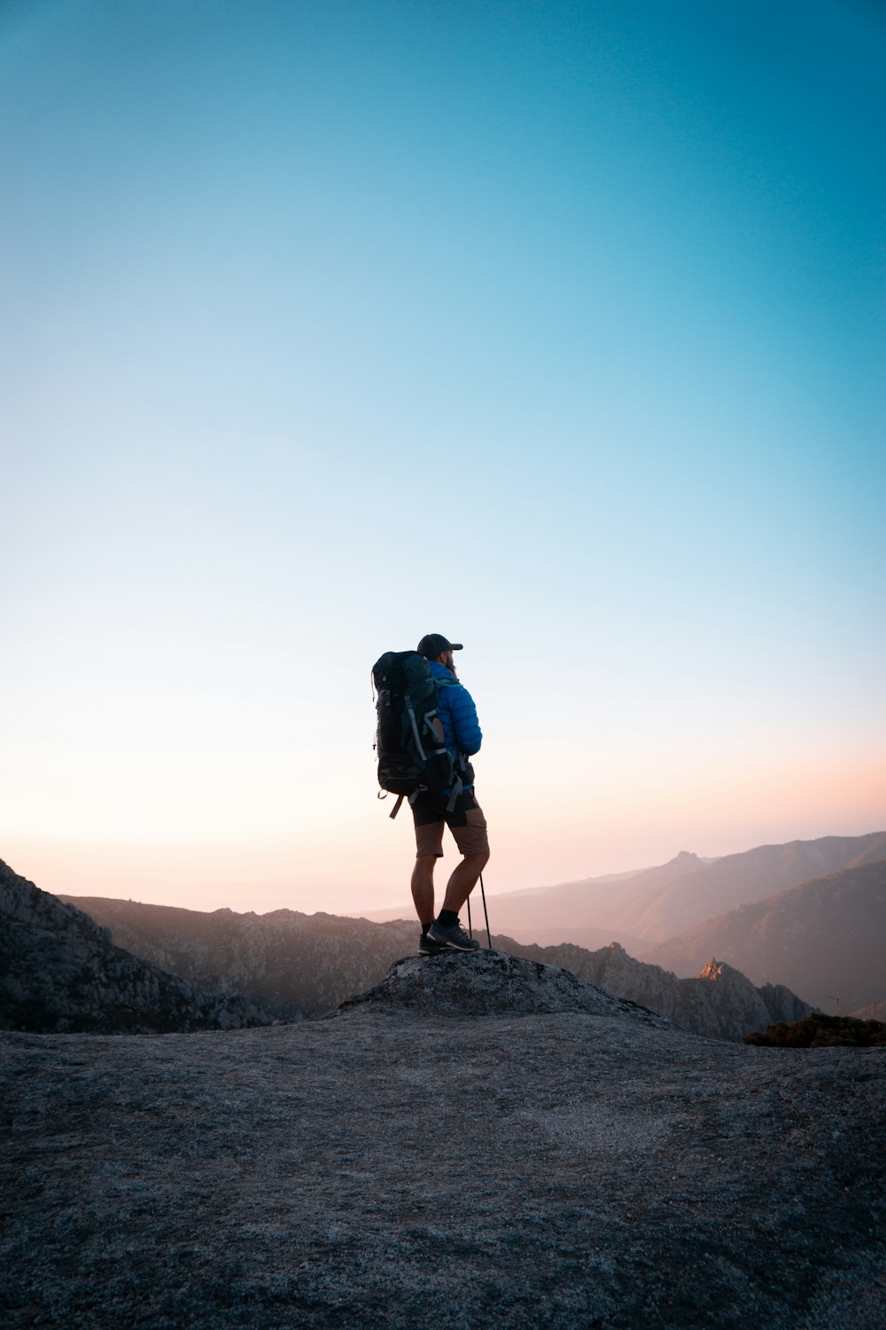 uomo in giacca nera e pantaloncini di jeans blu con zaino da trekking nero in piedi sulla montagna durante