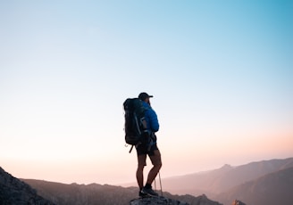 man in black jacket and blue denim shorts with black hiking backpack standing on mountain during