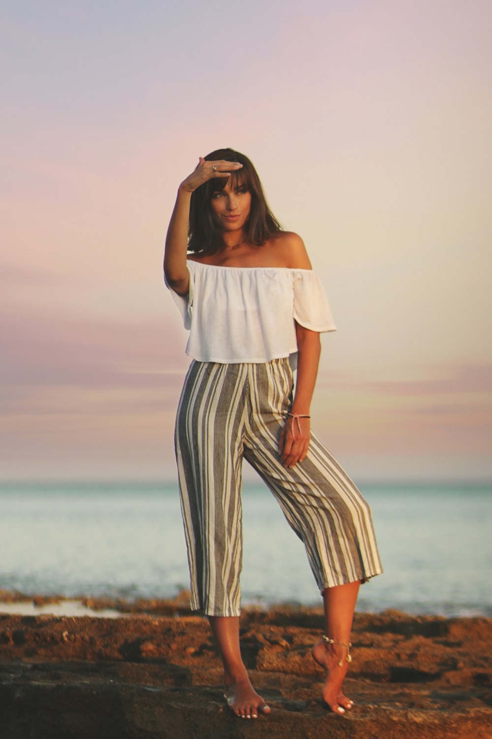 woman in white sleeveless shirt and black and white striped pants standing on beach during daytime