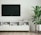 A minimalist living room setup features a wall-mounted flat-screen TV above a sleek, white console table. Decorative books and a small plant in a vase adorn the table, alongside a modern geometric sculpture. The area is complemented by a tall potted plant, adding a touch of greenery to the decor.