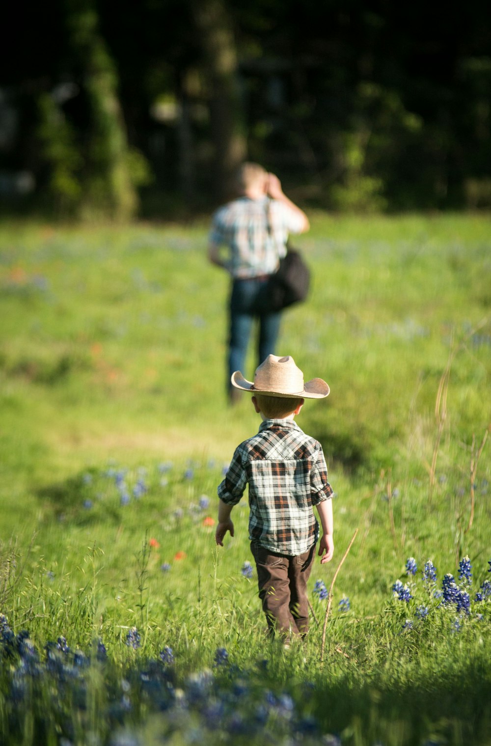 child in blue and white plaid dress shirt wearing brown hat standing on green grass field