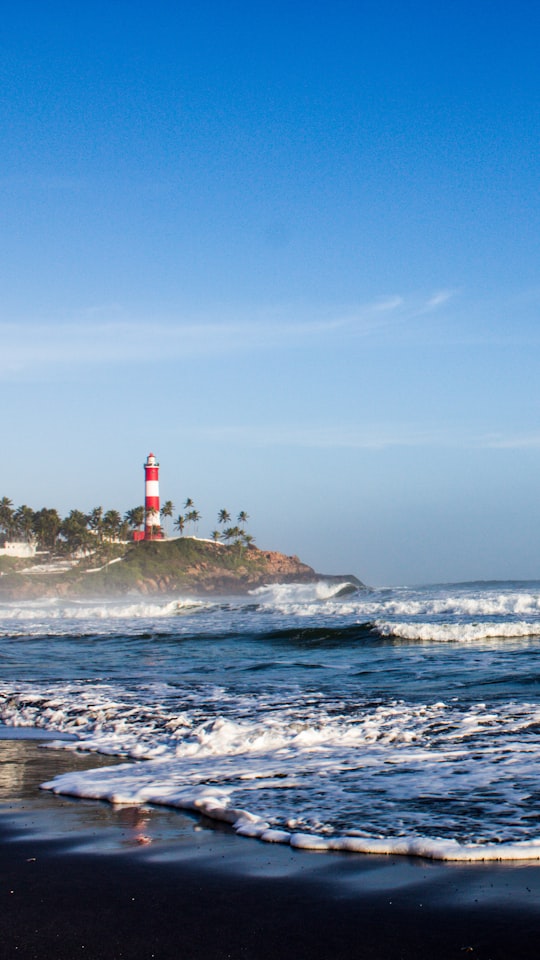 red and white lighthouse on rock formation near sea during daytime in Kovalam India