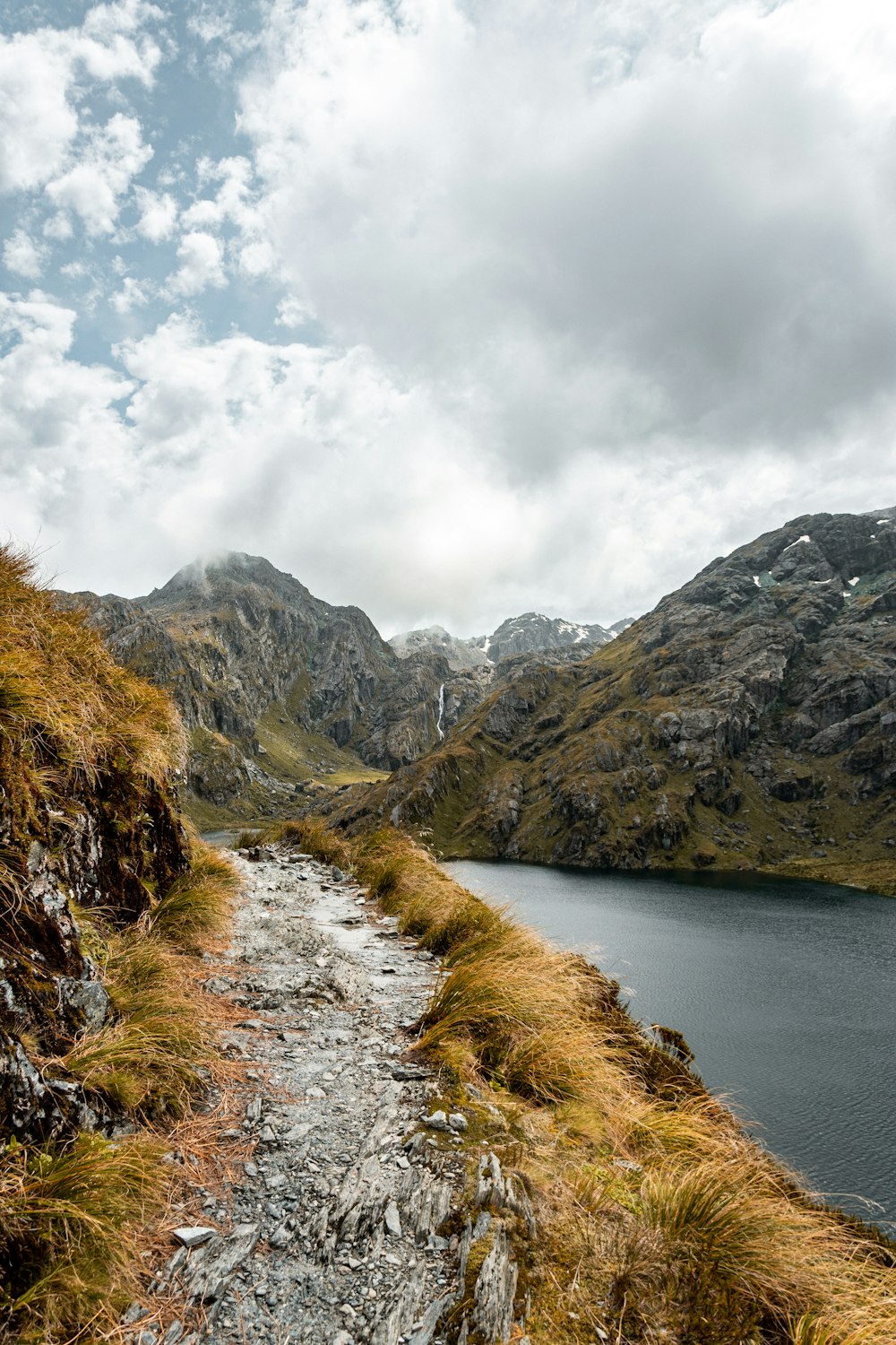 montagna verde e marrone accanto al fiume sotto le nuvole bianche durante il giorno