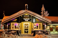 A cozy mountain lodge glowing warmly as night falls, with people enjoying drinks outside.